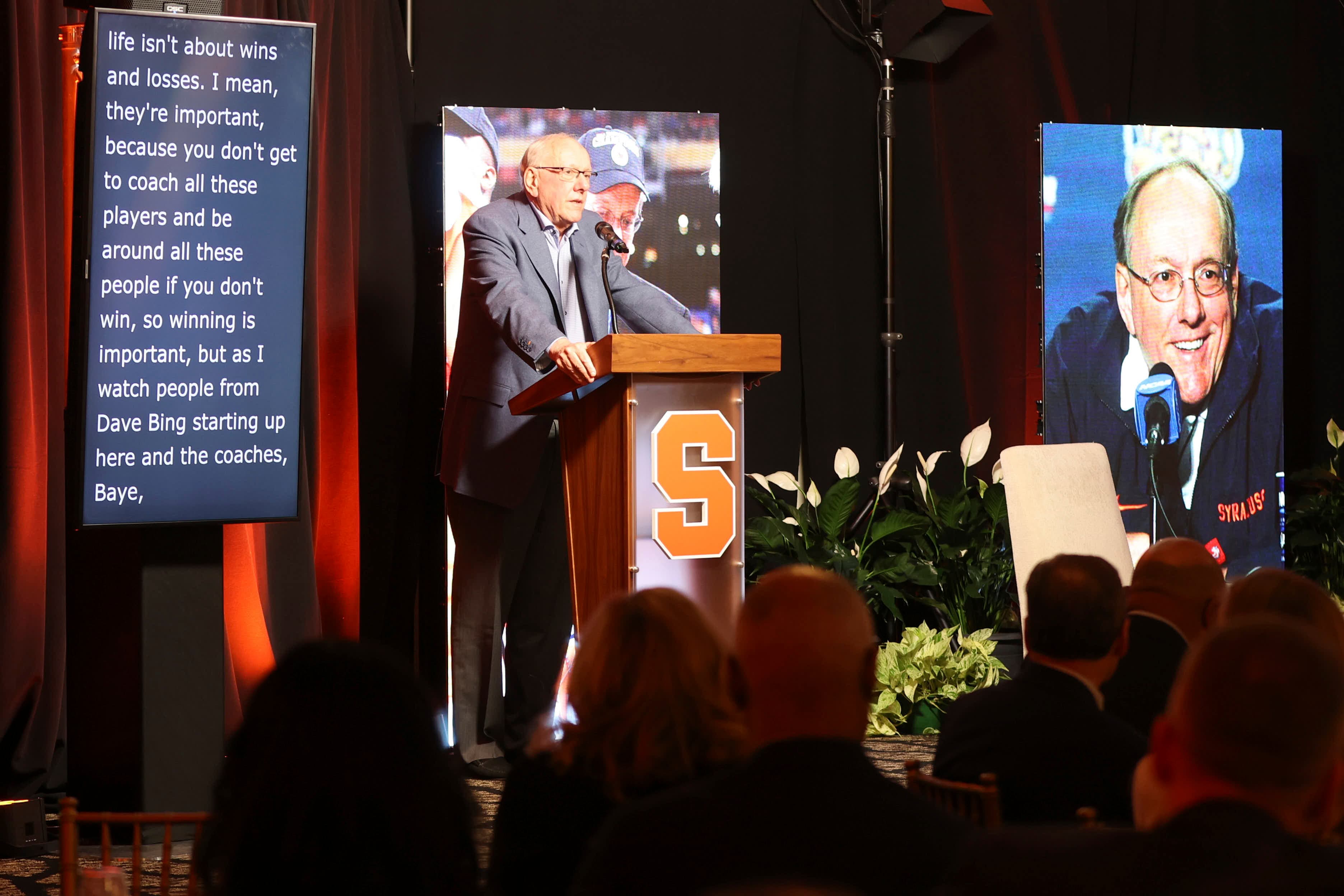 Awards speaker at a podium framed by vertical video displays
