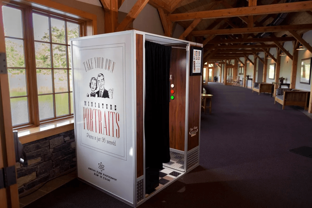 The classic Miniature Portraits photo booth set along a wall in a timber-frame venue hallway