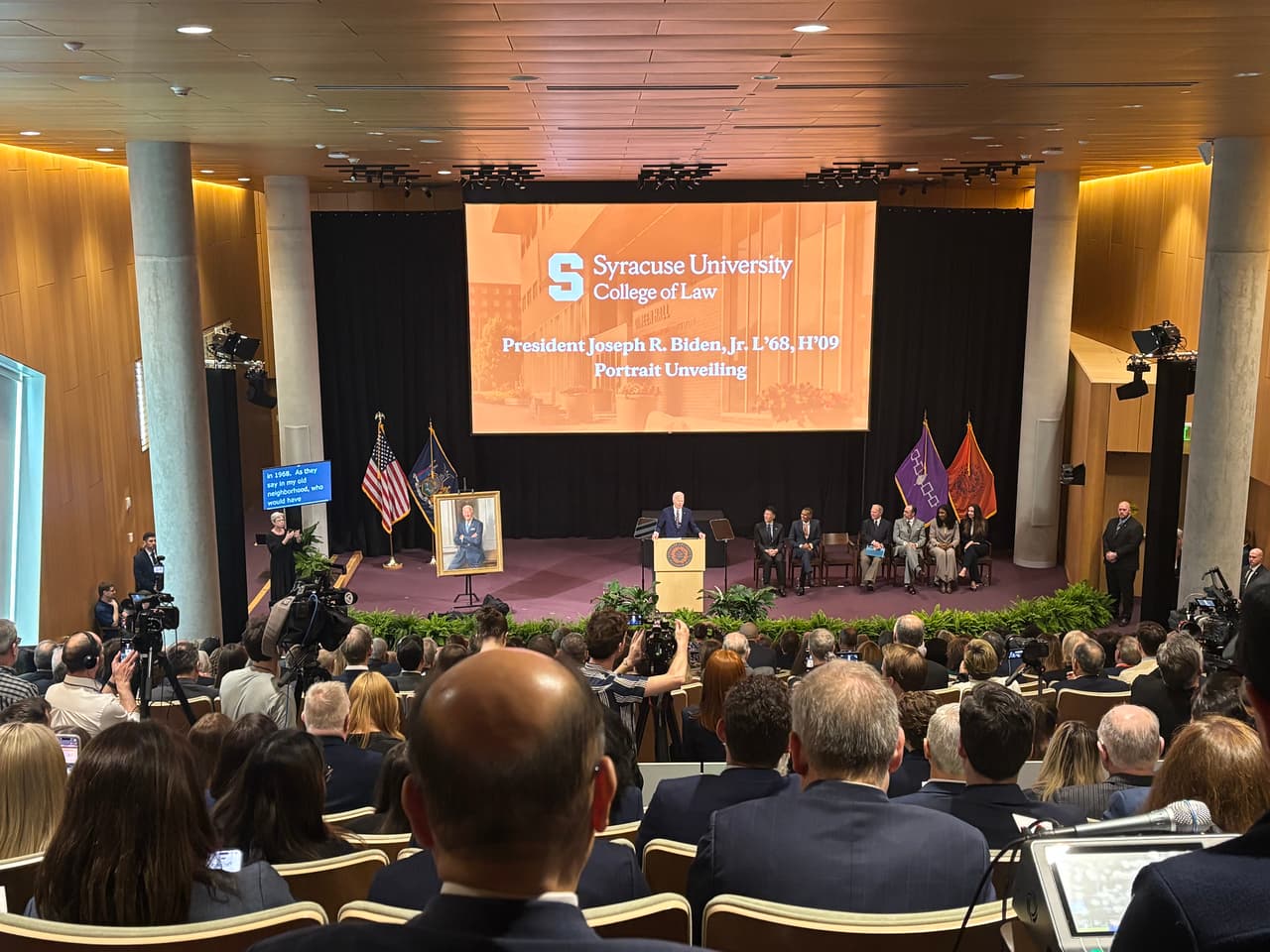 University auditorium presentation with stage projection and media coverage