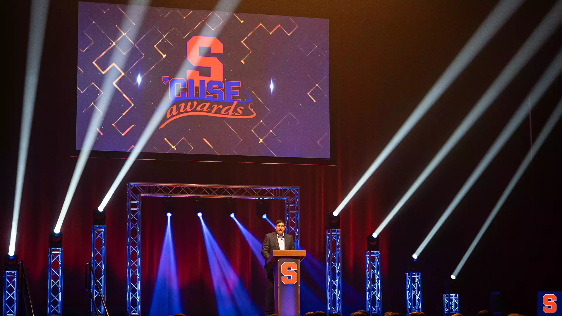 Awards program stage with a presenter, projection, truss, and moving lights