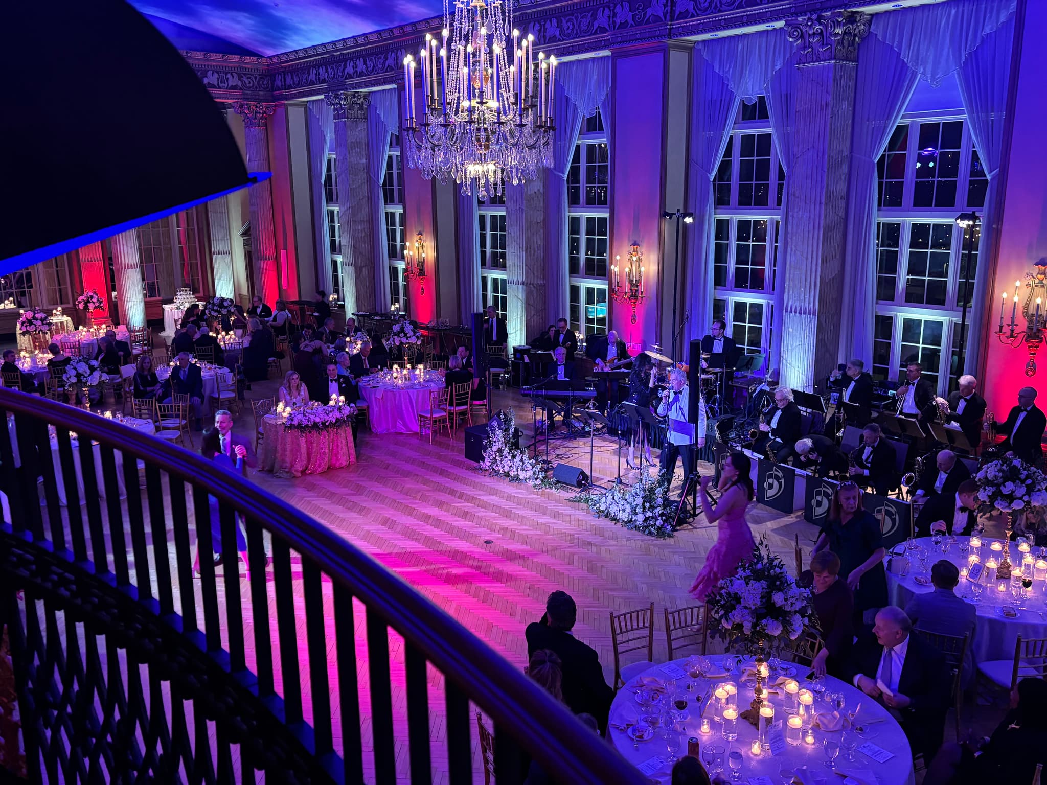 A formal ballroom event with architectural lighting, a live band, and guest tables